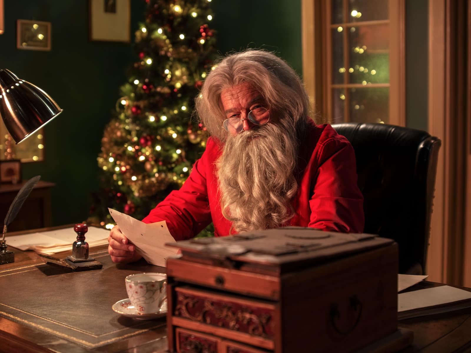 Santa at his desk in the North Pole, reading a Nice List nomination letter by lamplight